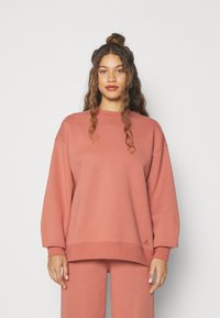 Sudadera de gran tamaño en rosa empolvado, hecha de una tela suave. Presenta mangas largas, puños acanalados y un pequeño logo en el dobladillo. Diseño casual.