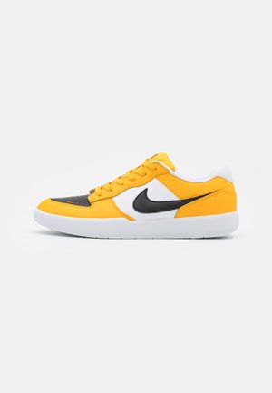 Niski sneaker w kolorze żółtym i białym z czarnym noskiem i logo Nike Swoosh, płaska biała podeszwa oraz zapięcie na sznurowadła, widok z boku na białym tle.
