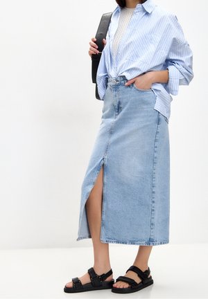 Light blue striped shirt over a light wash denim maxi skirt with a front slit, paired with black sandals and a black shoulder bag.