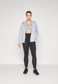 Fato de capuz cinza com fecho, top cropped cinza claro, leggings pretas de cintura alta com detalhes em texto e ténis pretos; tecido suave e ajuste atlético.