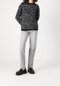 Schwarzer und grauer Leo-Print-Pullover, lockere Passform; kombiniert mit hellgrauen, gerade geschnittenen Jeans und klobigen schwarzen Schuhen. Weißer Hintergrund.