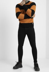 Oranssi-musta raidallinen neulepaita, jossa on resorikuosi. Yhdistetty mustiin slim-fit-farkkuihin ja mustiin urheilukenkiin.