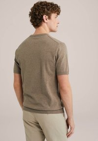 Short-sleeve, olive-green knit sweater with a crew neckline, textured fabric, and ribbed hem. Worn with light-colored trousers.