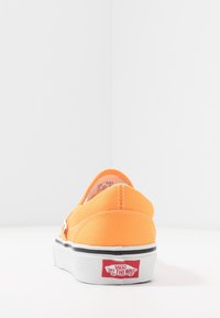 Chaussure orange en toile sans lacets avec une semelle en caoutchouc blanche et des accents noirs. Comprend le logo Vans sur le talon et des détails cousus.