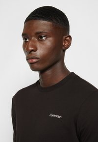 Zwarte katoenen t-shirt met ronde hals, met een witte geborduurde "Calvin Klein" logo aan de linkerzijde van de borst. Korte mouwen, minimalistisch ontwerp.