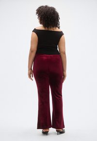 Fekete, váll nélküli felső bordó bársony színű, bővülő szárú nadrággal, sima textúrával és testhezálló derékkal. A megjelenést magas sarkú cipő egészíti ki.