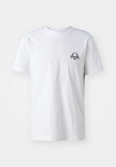 Baltas kokvilnas T-krekls ar nelielu melnu izšūtu dizainu uz krūtīm; īsas piedurknes un klasiska apļa kakla stils.