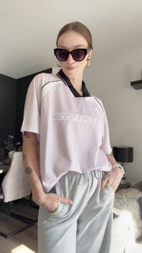 T-shirt oversize rosa con colletto nero e stampa "LETSFRAN", abbinata a pantaloni felpati grigi chiari, dotati di tasche laterali e vestibilità comoda.