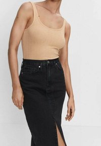 Béžový žebrovaný top bez rukávů kombinovaný s černou džínovou sukní s vysokým pasem, která má přední rozparek a jemné švy.