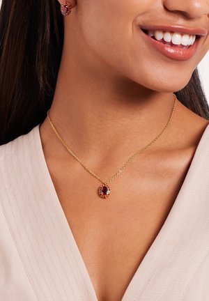 Gouden ketting met een delicate schakel, voorzien van een ovale paarse hanger omringd door kleine oranje edelstenen. Gladde textuur, elegante ontwerp.
