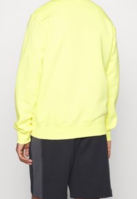 Neon gul sweatshirt med långa ärmar och ribbade muddar. Har en rund halsringning och en avslappnad passform. Matchas med mörka shorts.