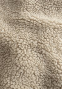 Beige, textured fleece stof med en blød, fluffy overflade. Har et bølget mønster og en let variation i farvetone.