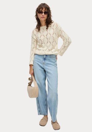 Cream-colored knit sweater with diamond pattern, paired with light blue high-waisted jeans and beige slides. Holding a beige handbag.