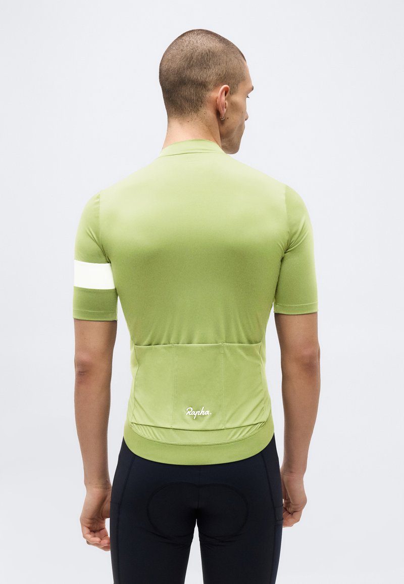 Mann trägt ein hellgrünes kurzärmeliges Radtrikot mit einem weißen Streifen am Arm und schwarze Radhose, von hinten gesehen.