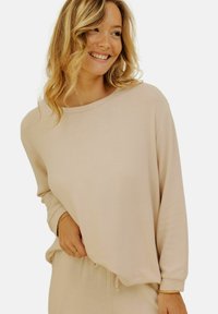 Sweatshirt beige  à manches longues en tissu doux, avec une coupe ample, un col rond et une texture subtile. Assorti à un pantalon coordonné.