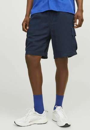 Pantalones cortos de carga en color navy con bolsillos laterales, fabricados en una tela ligera. Combinados con zapatillas deportivas blancas y calcetines de canalé azules.