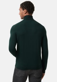 Dark green turtleneck sweater with a fitted design, ribbed collar, and cuffs. Soft texture and seamless shoulders, paired with gray jeans.