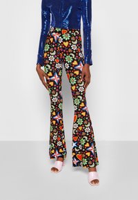 Pantalones ajustados de campana negros con patrones coloridos de flores, estrellas y corazones; combinados con una blusa larga de manga brillante azul y tacones rosa destalonados.