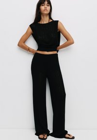 Completo in maglia nero composto da top senza maniche con scollatura ampia e pantaloni a vestibilità morbida. Tessuto testurizzato con righe verticali.