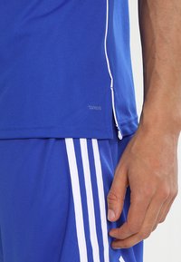 Blauses Sportshirt mit weißen Akzenten, strukturierter Stoff und seitlichem Schlitz. Verfügt über ein Etikett mit "Climacool". Passende Shorts haben weiße Streifen.