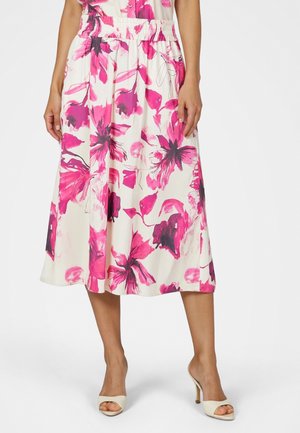 Woman wearing a white midi skirt with bright pink and dark floral patterns, paired with white open-toe high-heeled shoes.