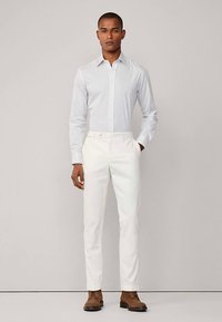 Ljusblå randig långärmad skjorta kombinerad med vita byxor och bruna läderskor. Enkelt design, figursydd form, mjuk textur.