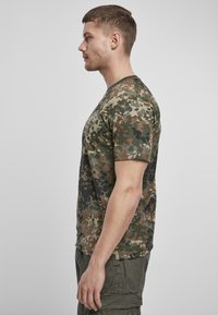 Kareivinių šortų rankovių t-shirt'as, kuriame derinami žali, rudi ir juodi raštai; medvilninis audinys; apykaklė apvaliu iškirpimu; laisvas fasonas; parodyta šoninė perspektyva.