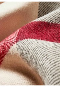 Tissu en laine douce avec un motif tartan beige, rouge et gris montrant la texture et les fibres en gros plan.