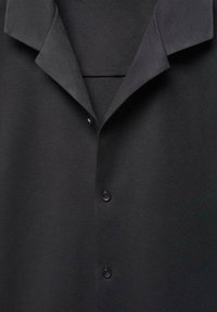 Camicia nera con colletto e tre bottoni neri visibili, realizzata in un tessuto morbido e testurizzato, mostrata da vicino frontalmente.