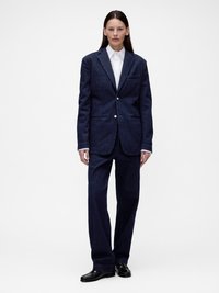 Σκούρο τζιν σακάκι με γλώσσες στο πέτο και μία μπροστινή τσέπη, συνδυασμένο με ταιριαστό φαρδύ παντελόνι. Λευκό πουκάμισο με γιακά από μέσα.