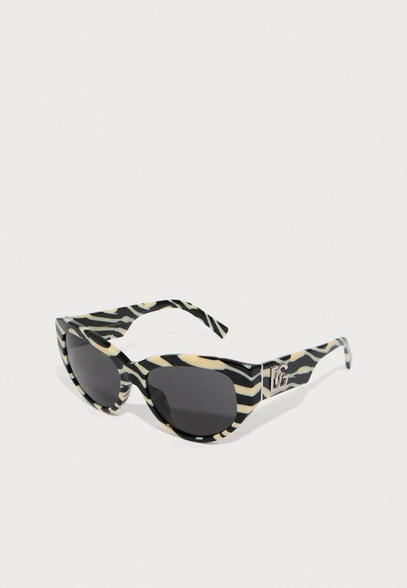 Sluneční brýle s číslem zebra v černé a krémové barvě, s oversized rámy, tmavými skly a logem na nožičce. Lesklý povrch, elegantní tvar.