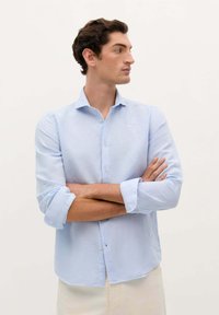 Camicia azzurro chiaro con bottoni, realizzata in un tessuto morbido, dotata di colletto, maniche lunghe arrotolate ai polsini e orlo curvo.