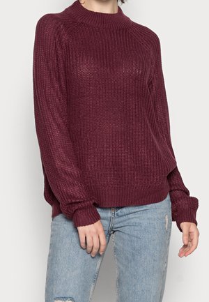 Maglione lavorato a maglia color bordeaux con colletto alto e polsini a costine; presenta una vestibilità ampia e un tessuto testurizzato con un motivo di piccoli fori.