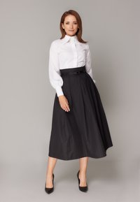 Biała bluzka z długim rękawem o wysokim kołnierzu, połączona z czarną plisowaną spódnicą midi z paskiem i pionowymi prążkami. Czarne szpilki.
