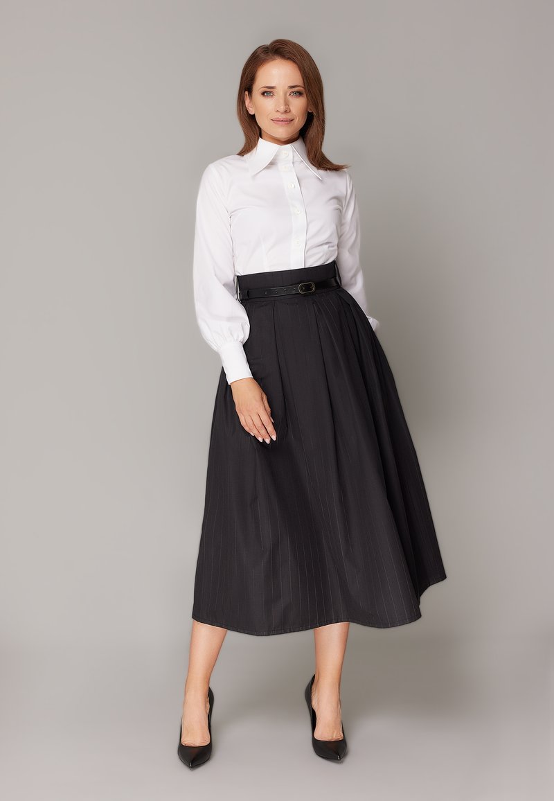 Biała bluzka z długim rękawem o wysokim kołnierzu, połączona z czarną plisowaną spódnicą midi z paskiem i pionowymi prążkami. Czarne szpilki.