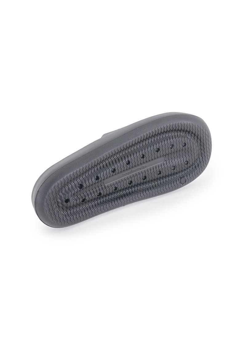 Suola di scarpa in gomma grigia con superficie texture, perforazioni circolari e scanalature orizzontali; progettata per trazione e stabilità.
