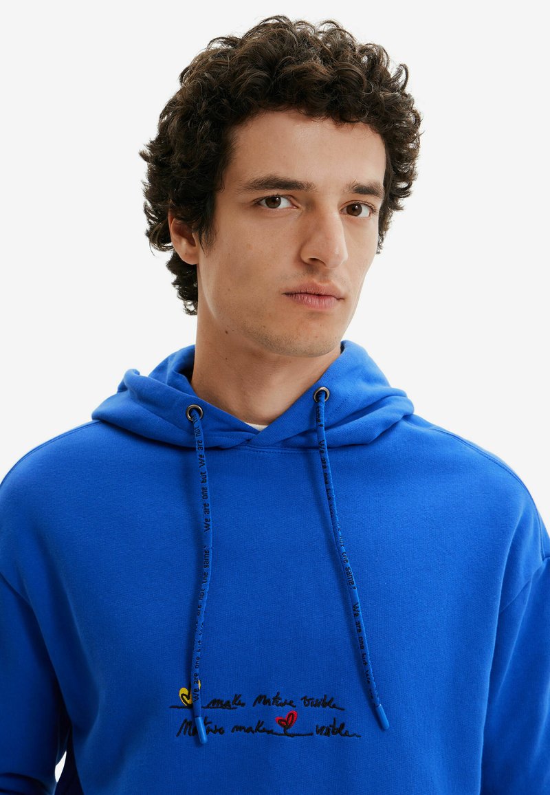 Niebieska bluza z kapturem, wykonana z bawełny, z regulowanym sznurkiem, haftowanym tekstem oraz grafikami w kolorze żółtym, czerwonym i czarnym z przodu.