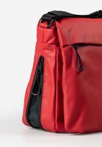 Borsa rossa con un'esterno liscio, tasca con zip nera e tracolla regolabile. Presenta un design elegante e angolare.