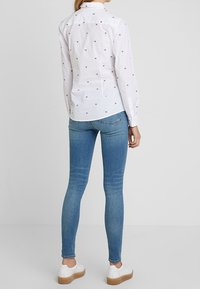 Camisa blanca de botones con pequeños patrones rojos y azules, combinada con jeans ajustados azules y zapatillas blancas con una suela de plataforma marrón claro.