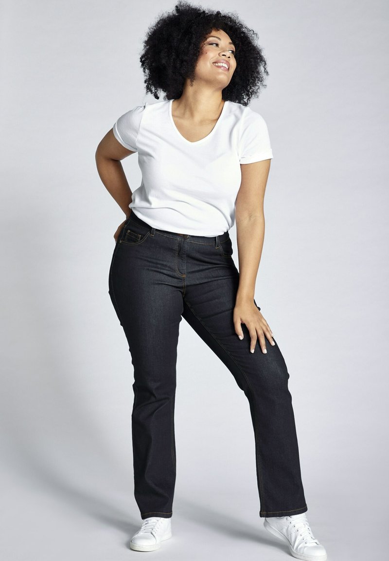 Tmavé denimové džínsy so priliehavým strihom, kontrastným prešívaním a klasickým strihom, skombinované s jednoduchým bielym tričkom s výstrihom do V a bielymi teniskami.