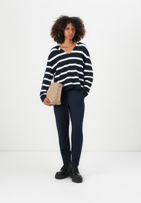 Marineblå og hvite stripete oversized genser, V-halsdesign. Kombinert med marineblå bukser og svarte chunky støvler. Holder en beige toalettmappe.