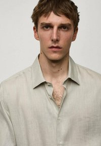 Camicia in lino beige chiaro con design a bottoni e colletto rilassato. Presenta una texture sottile e dettagli di cucitura visibili.