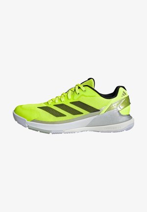 Helle gelbe Sportschuhe mit einem Obermaterial aus Mesh, schwarzen Akzenten, drei diagonalen Streifen und einem silbernen Fersenbereich sowie einer weißen Zwischensohle.
