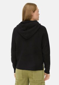 Zwarte, met een textuur gebreide hoodie, met lange mouwen en zijsplitten, gecombineerd met olijfgroene cargobroek.
