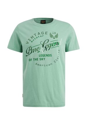 Camiseta de algodón verde claro con cuello redondo; presenta texto y gráficos impresos en verde oscuro y blanco, incluyendo "Vintage Aviator" y "Legends of the Sky."