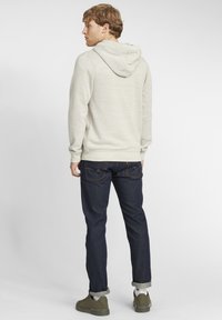 Lysegrå hættetrøje med struktureret overflade, parret med mørke denim jeans og grønne støvler. Afslappet og løs pasform med optrillede ærmer.
