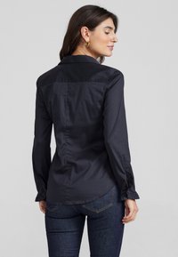 Zwarte, knoopsluiting shirt met een soepele textuur, voorzien van een kraaghalslijn, lange mouwen met gerimpelde manchetten en een getailleerde pasvorm.