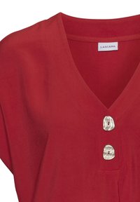 Rote Bluse mit V-Ausschnitt, kurzen Ärmeln und zwei dekorativen, runden, perlenähnlichen Knöpfen auf der Vorderseite. Weicher Stoff.