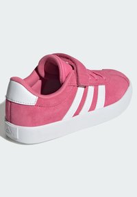 Zapatilla de ante rosa con rayas blancas, puntera redondeada y suela de goma texturizada. Presenta una correa de gancho y bucle para un fácil ajuste.