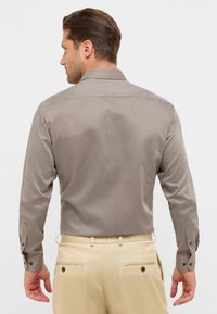 Langsleeve shirt in een bruine geometrische print, gemaakt van gladde stof, met een kraag en knoopmanchetten, gecombineerd met beige broeken.